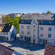eit dronebilde av bygninger i Florø. eit stort, rosa gamalt bygg står i front av bilde. ein person syklar med vogn nede i gata. det er blå himmel
